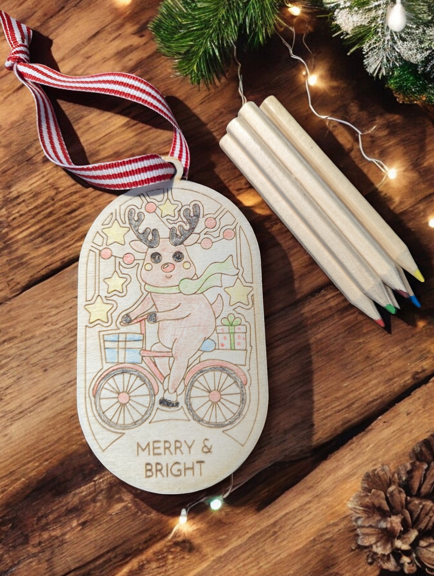 Wooden laser engraved ornament with outline of reindeer bicycling. Colored pencils stacked in the background.